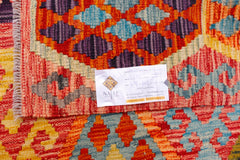 A handwoven Afghan Maimana kilim featuring a vibrant geometric pattern in red, blue, and purple.