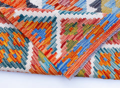 A folded Afghan Maimana kilim rug featuring vibrant geometric patterns in wool.