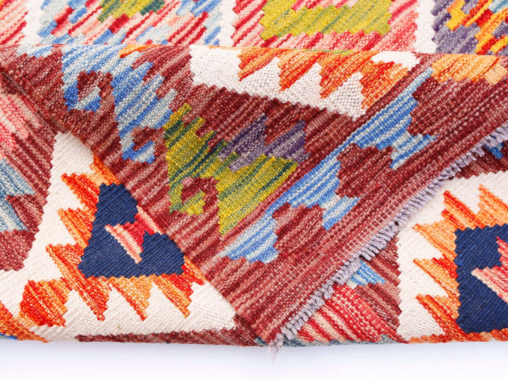 A folded handmade Afghan Maimana kilim rug featuring vibrant geometric patterns in wool.