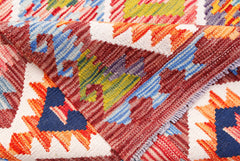 A folded handmade Afghan Maimana kilim rug featuring vibrant geometric patterns in wool.