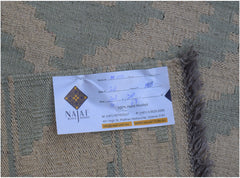 A flatwoven Afghan Maimana kilim rug featuring a geometric pattern in muted green and beige tones.