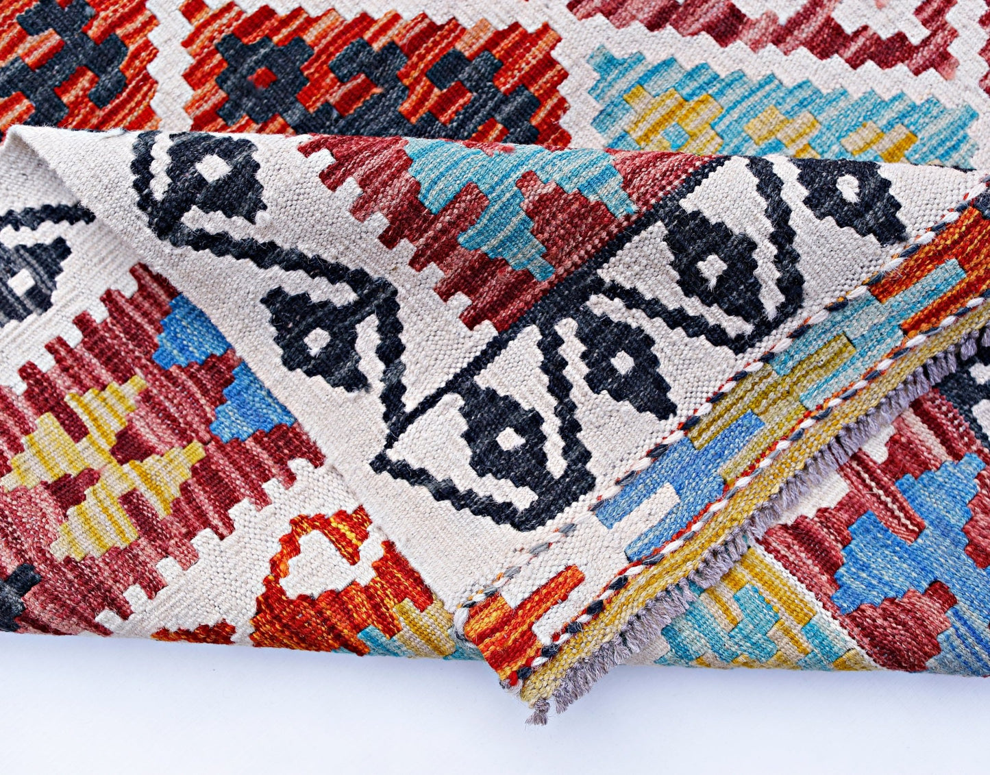 A folded Afghan Maimana kilim rug featuring a geometric pattern in red, blue, yellow, and black.