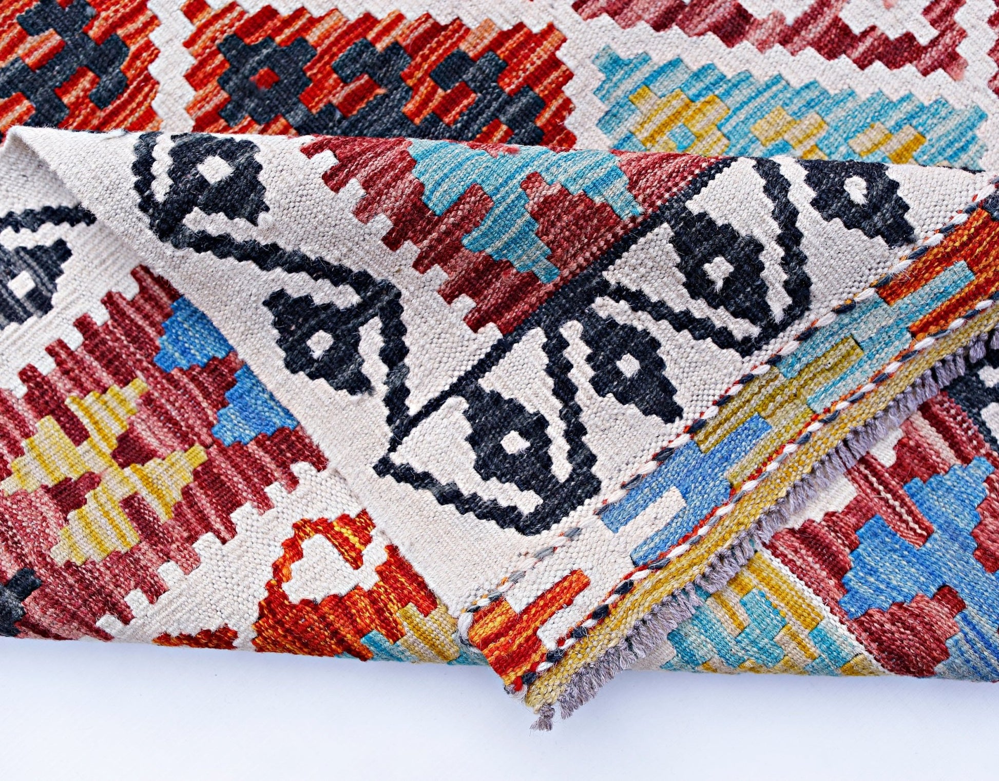 A folded Afghan Maimana kilim rug featuring a geometric pattern in red, blue, yellow, and black.