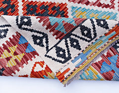 A folded Afghan Maimana kilim rug featuring a geometric pattern in red, blue, yellow, and black.