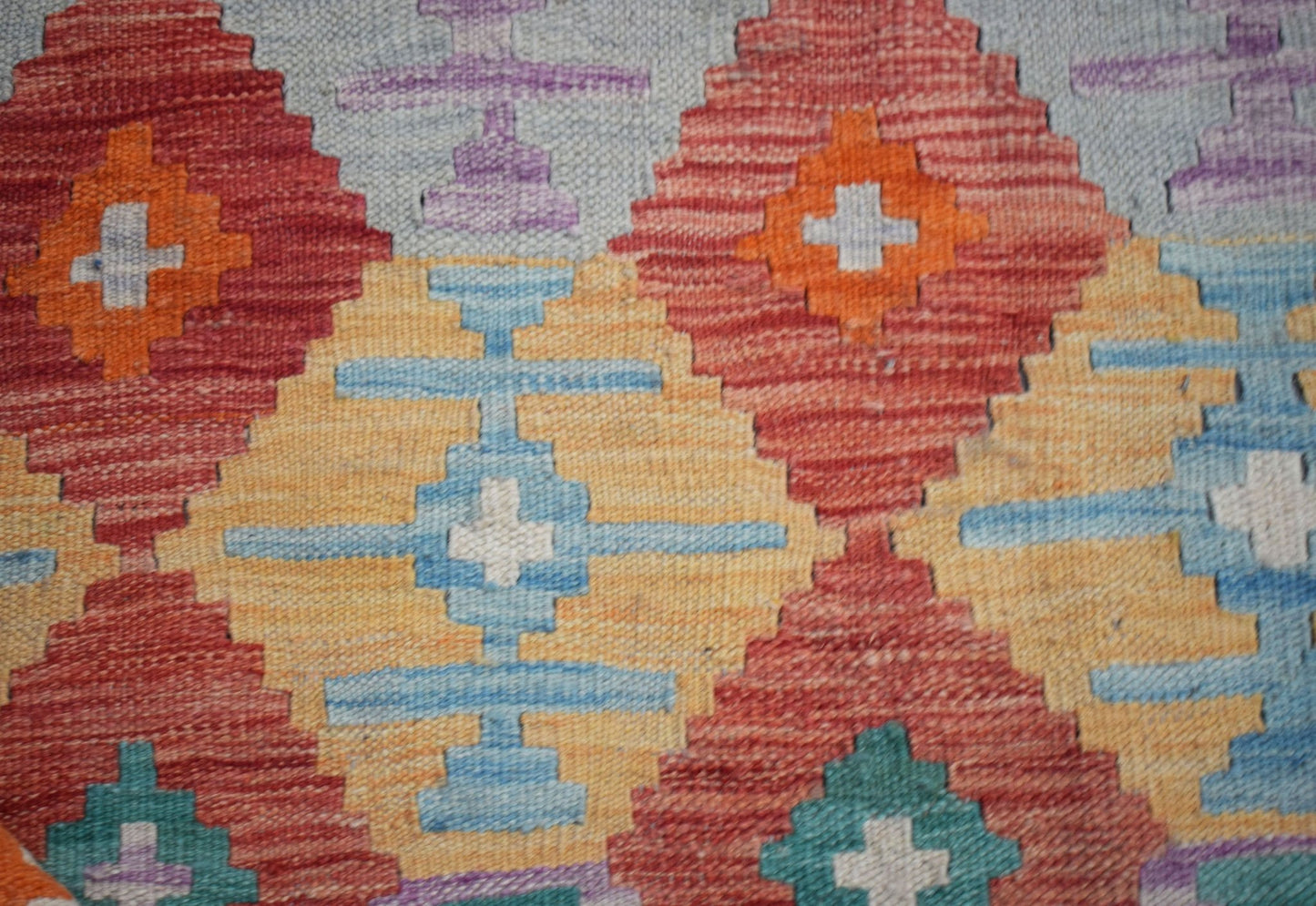 A handwoven Afghan Maimana kilim featuring a geometric pattern of diamonds in red, blue, and gold.