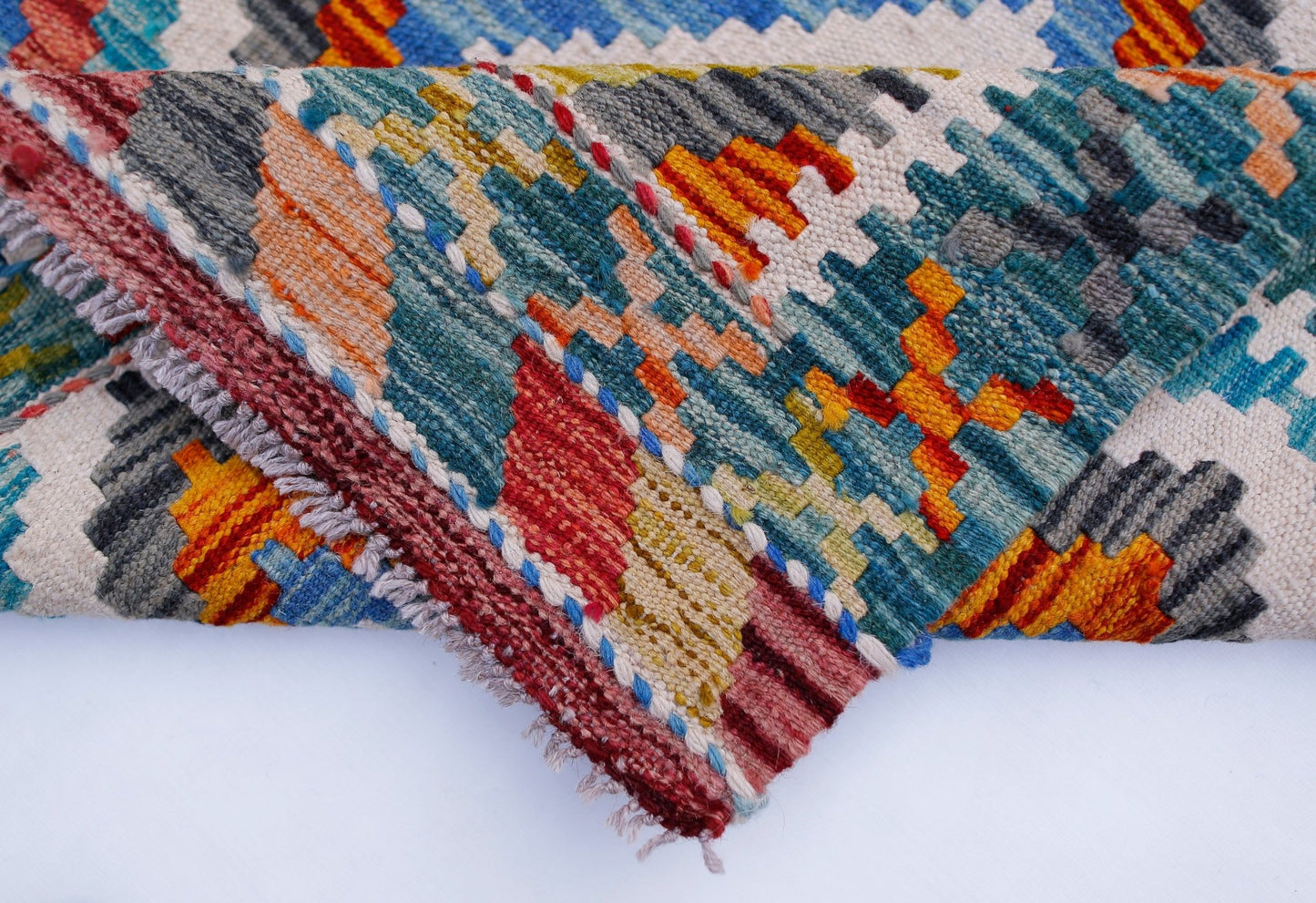 A folded Afghan Maimana kilim runner featuring a vibrant geometric pattern in wool.