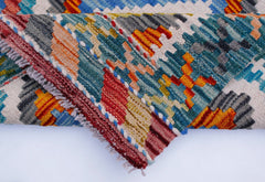 A folded Afghan Maimana kilim runner featuring a vibrant geometric pattern in wool.