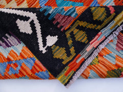 A folded Afghan Maimana kilim runner featuring vibrant geometric patterns in wool.