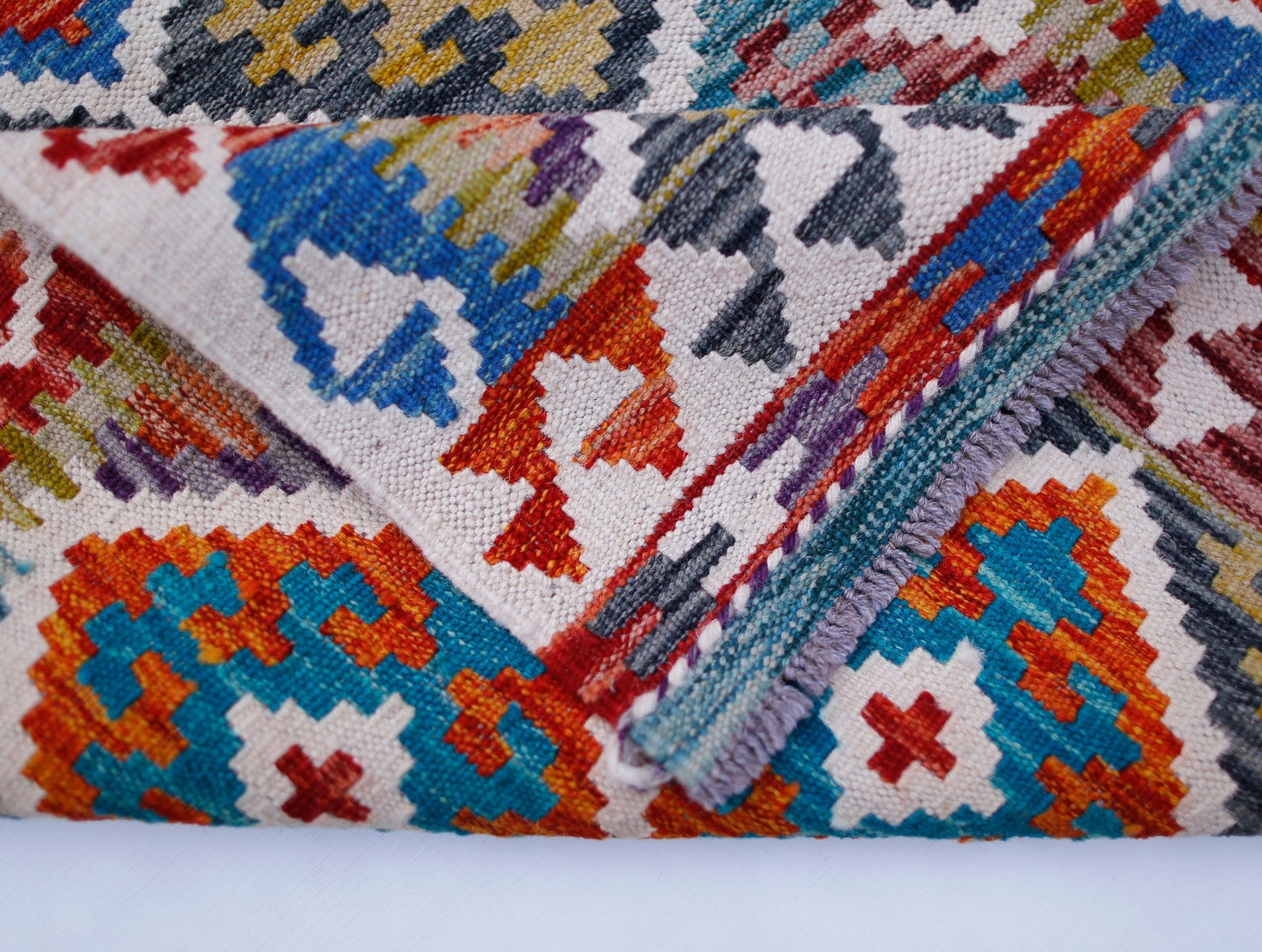 A folded Afghan Maimana Kilim runner featuring a vibrant geometric pattern in wool.