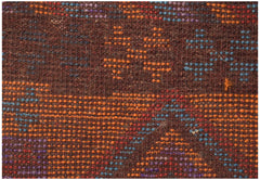 A close-up of a handmade Afghan wool rug featuring geometric patterns in orange, blue, and purple.