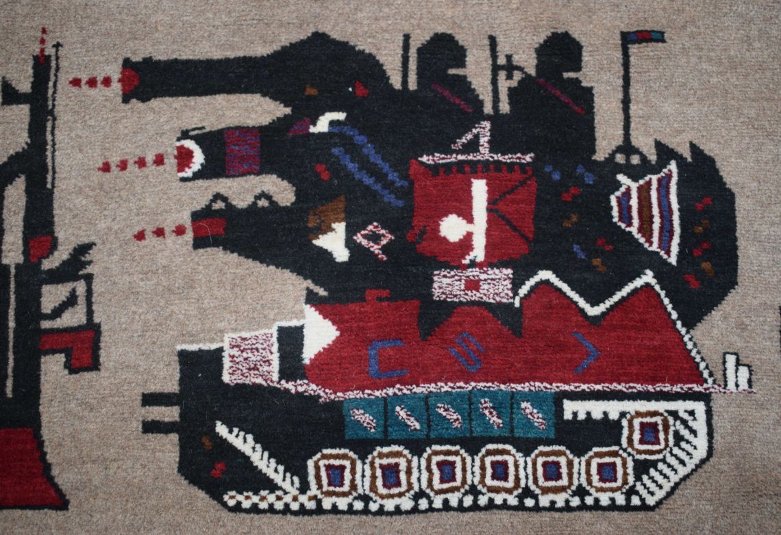 A handmade Afghan wool rug featuring a stylized black tank firing projectiles at a rifle.