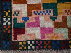 A handmade Afghan Pashm rug featuring a geometric pattern of colorful squares on a pink background.