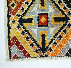 A hand-knotted Afghan wool rug featuring a bold geometric pattern in orange, yellow, and blue.