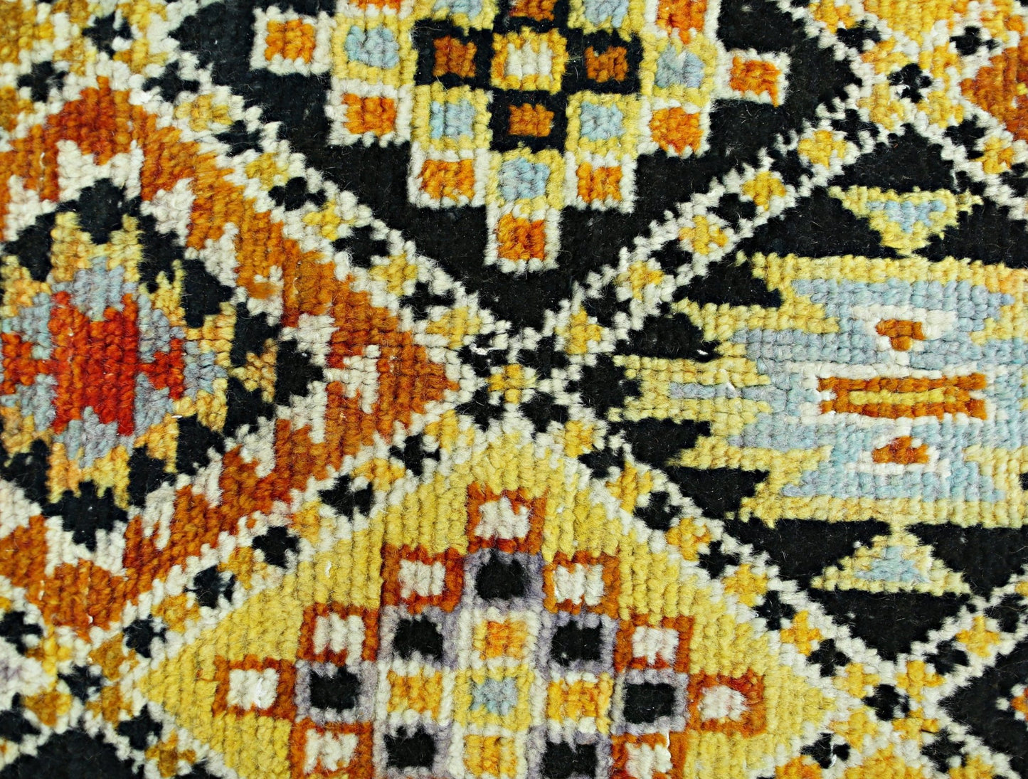 A hand-knotted Afghan wool rug featuring a bold geometric pattern in yellow, orange, and black.