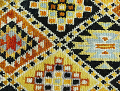 A hand-knotted Afghan wool rug featuring a bold geometric pattern in yellow, orange, and black.