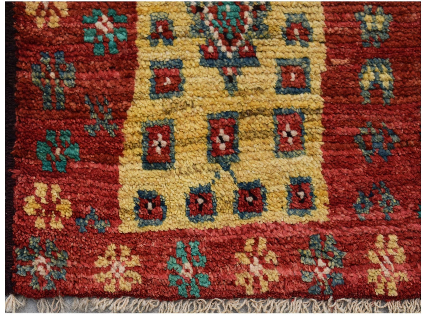 Hand-knotted Afghan wool rug featuring a red field with yellow geometric motifs and fringe ends.