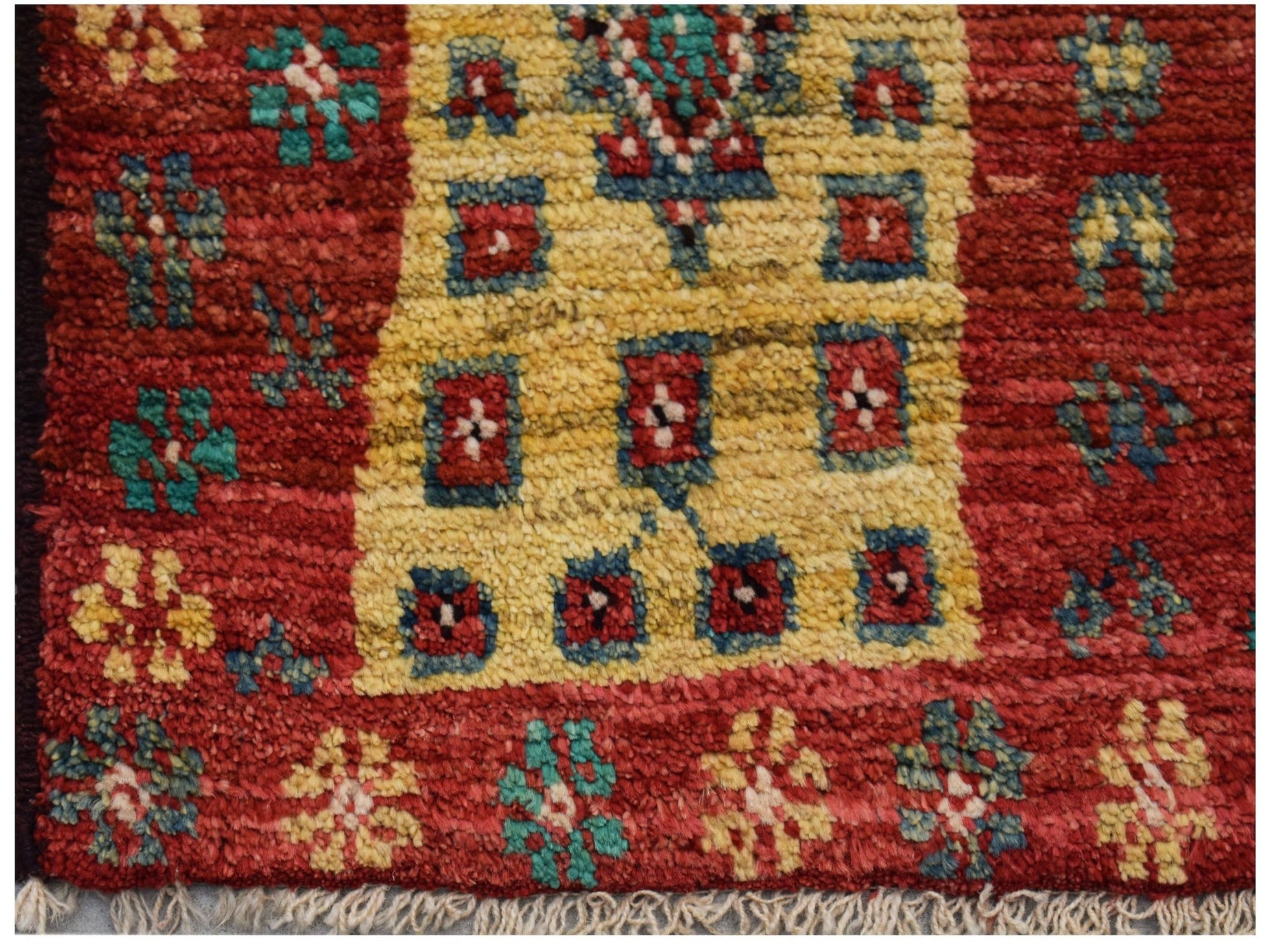 Hand-knotted Afghan wool rug featuring a red field with yellow geometric motifs and fringe ends.