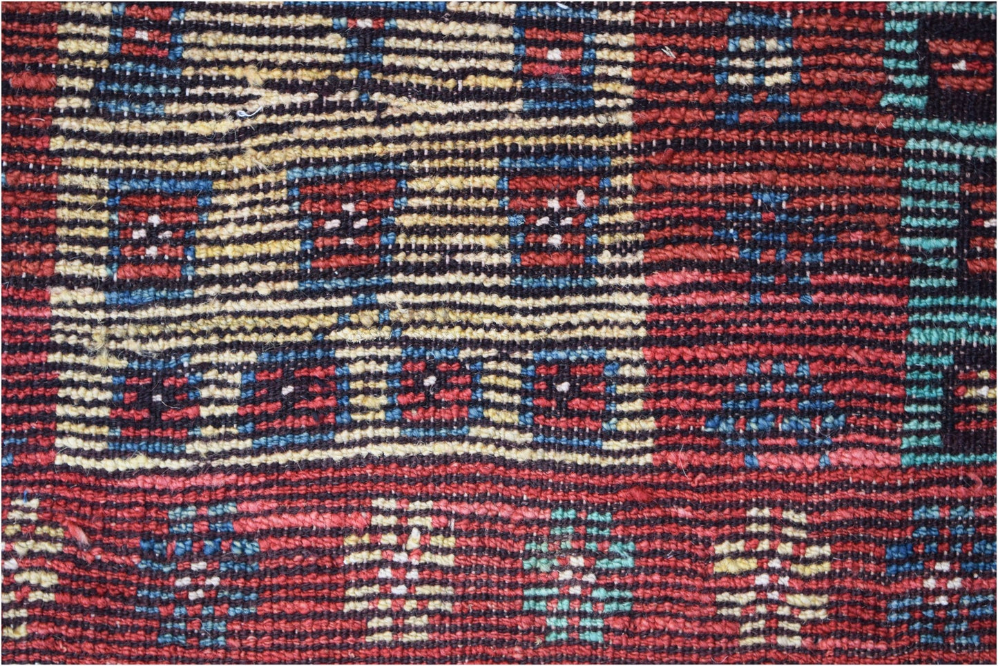 A hand-knotted Afghan wool rug featuring a geometric pattern in red, blue, yellow, and teal.