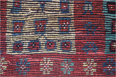 A hand-knotted Afghan wool rug featuring a geometric pattern in red, blue, yellow, and teal.