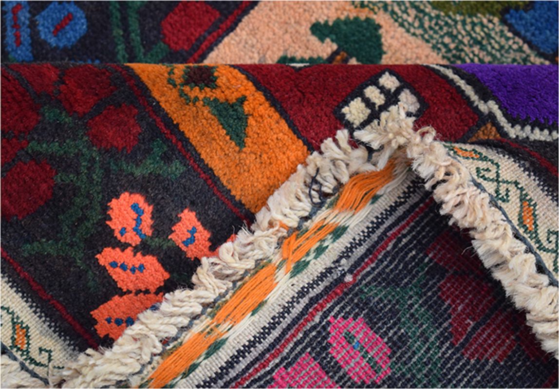 A folded handmade Afghan wool rug featuring vibrant tribal patterns in red, orange, and blue.
