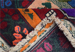 A folded handmade Afghan wool rug featuring vibrant tribal patterns in red, orange, and blue.
