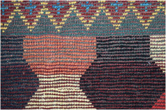 A close-up of a hand-knotted Afghan wool rug featuring geometric patterns in red, black, and yellow.