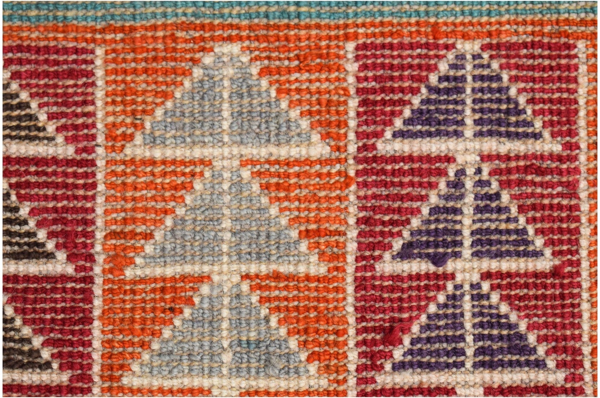 A close-up of a hand-knotted Afghan wool rug featuring geometric triangle patterns in vibrant colors.