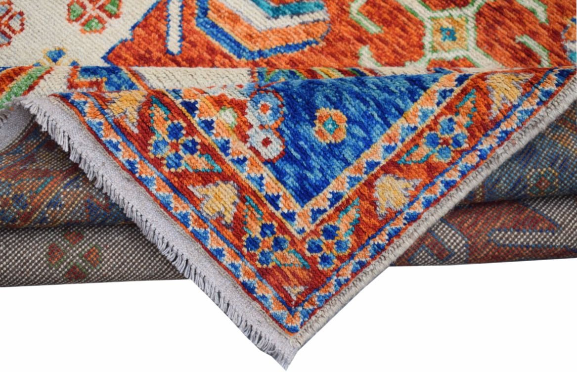 A folded handmade Afghan wool rug featuring a vibrant tribal pattern in blue, orange, and cream.