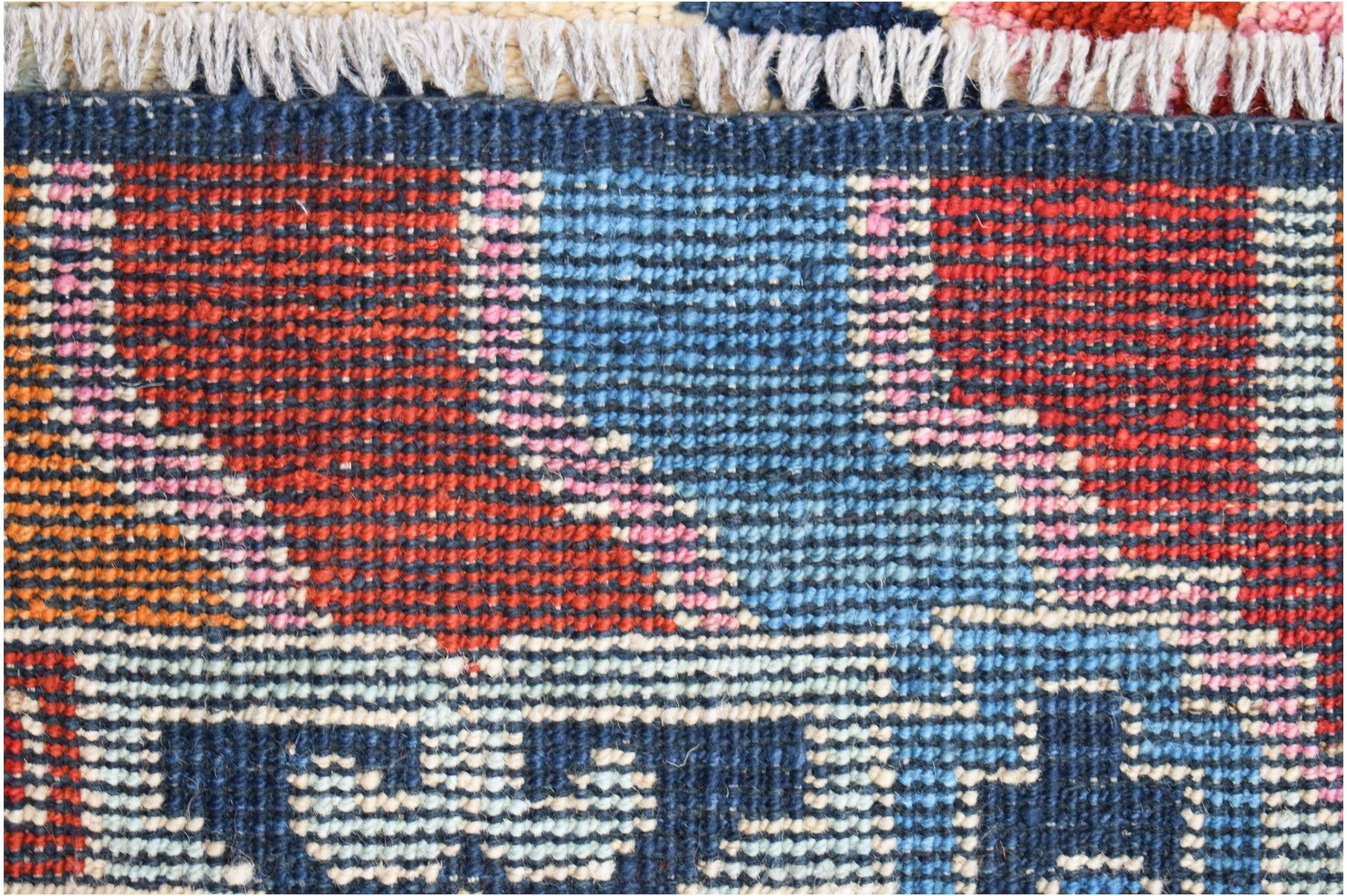 A close-up of a hand-knotted Afghan wool rug featuring bold geometric patterns in red, blue, and pink.
