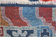 A close-up of a hand-knotted Afghan wool rug featuring bold geometric patterns in red, blue, and pink.