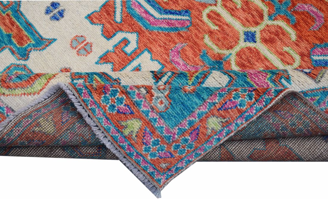 A handmade Afghan wool rug featuring a vibrant tribal pattern in orange, blue, and pink tones.