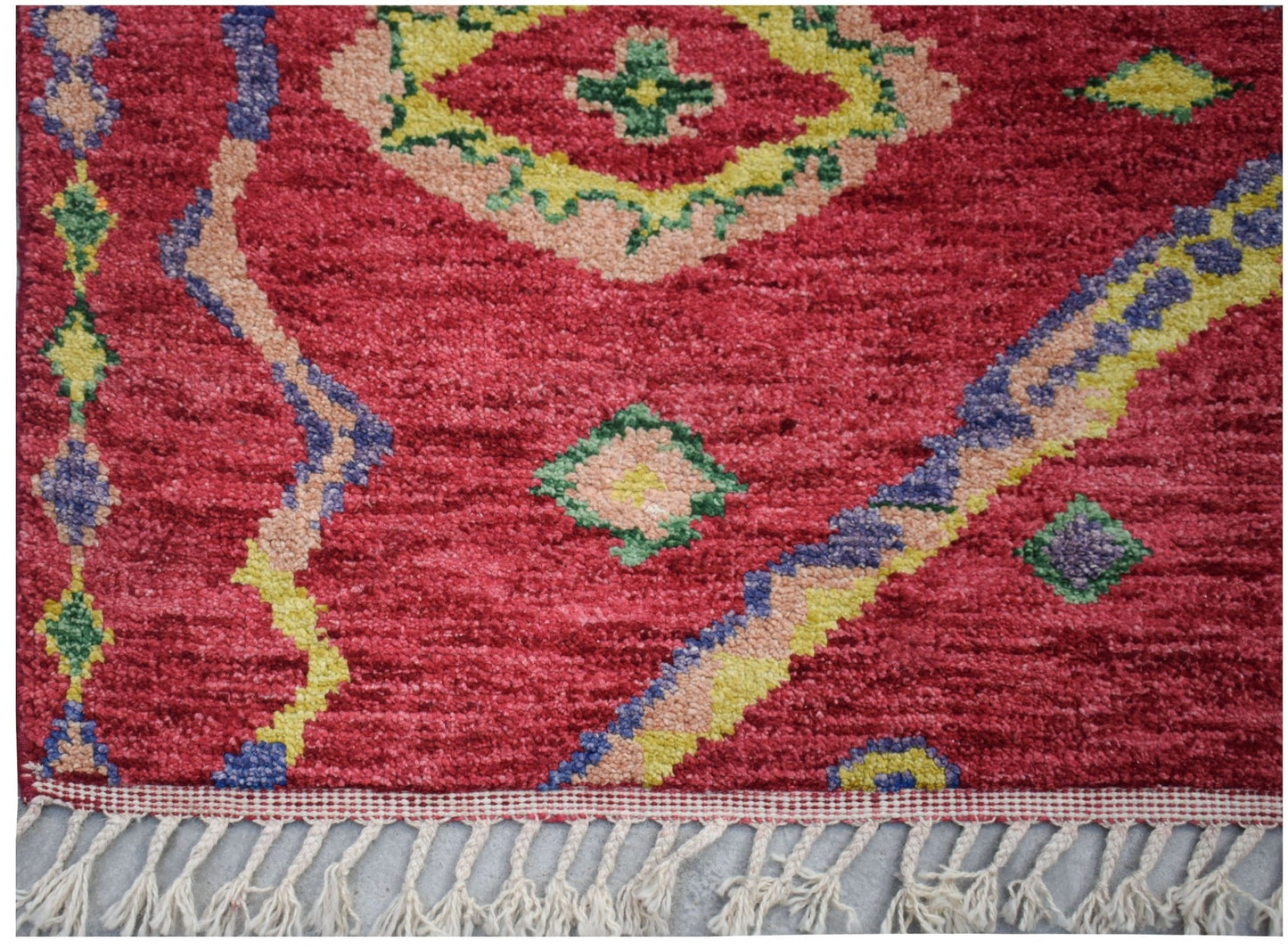 A hand-knotted Afghan wool rug featuring a vibrant red field with colorful geometric patterns.