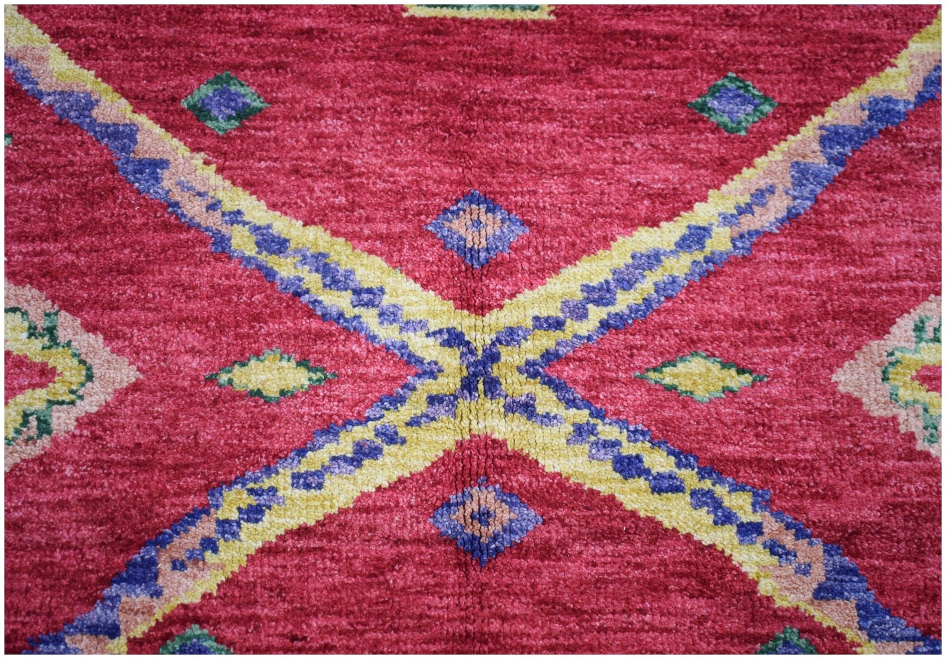 A handknotted Afghan wool rug featuring a vibrant red field with geometric blue and yellow patterns.