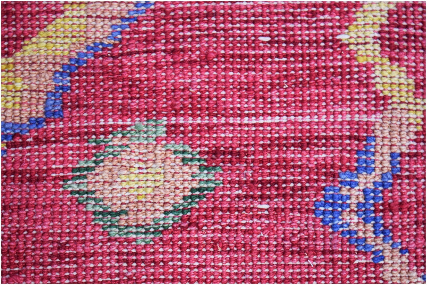A close-up of a hand-knotted Afghan wool rug featuring geometric patterns in red, blue, and yellow.