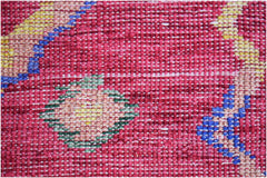 A close-up of a hand-knotted Afghan wool rug featuring geometric patterns in red, blue, and yellow.