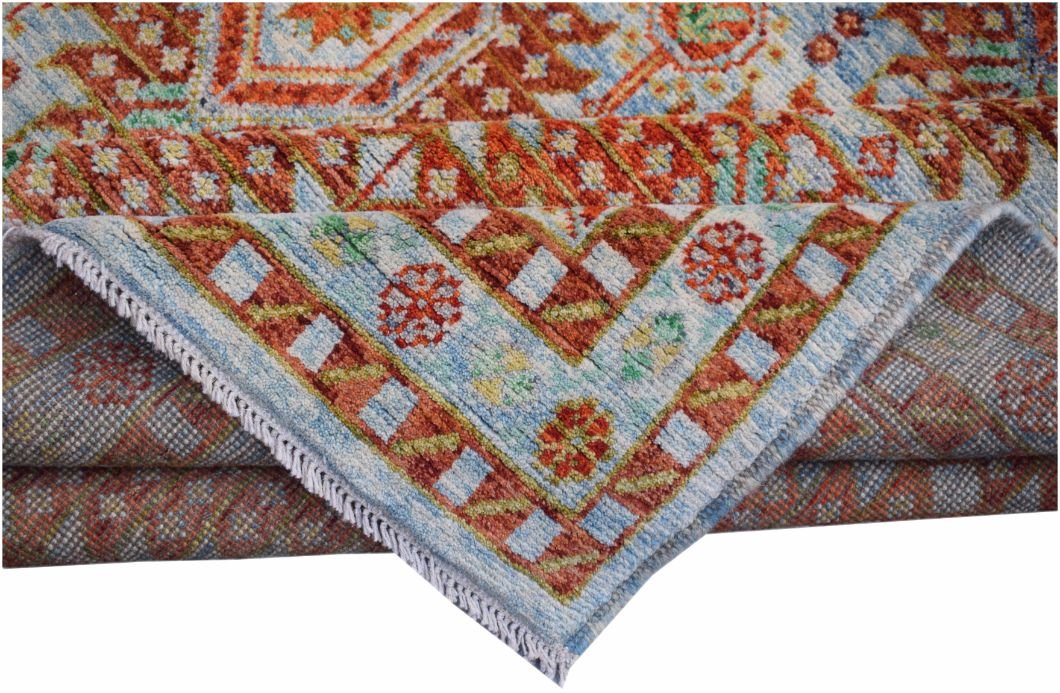A folded Afghan Pashm rug featuring a traditional tribal pattern in orange, blue, and green.