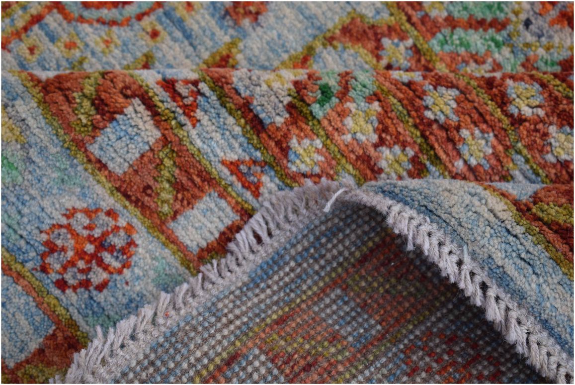 A close-up of a handmade Afghan wool rug featuring a colorful tribal pattern and fringed edges.