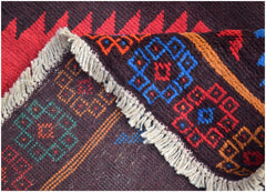 A close-up of a handmade Afghan wool rug featuring geometric patterns in red, blue, and orange.