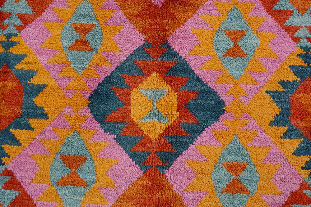 Handmade Afghan wool rug featuring a vibrant geometric diamond pattern in orange, pink, and blue.