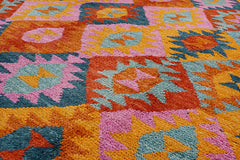 A handmade Afghan wool rug featuring a vibrant geometric pattern in orange, pink, and blue.