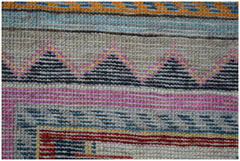 A close-up of a handmade Afghan wool rug featuring geometric patterns in pink, blue, and black.