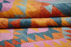 A handmade Afghan wool rug featuring a geometric pattern in shades of pink, blue, and orange.