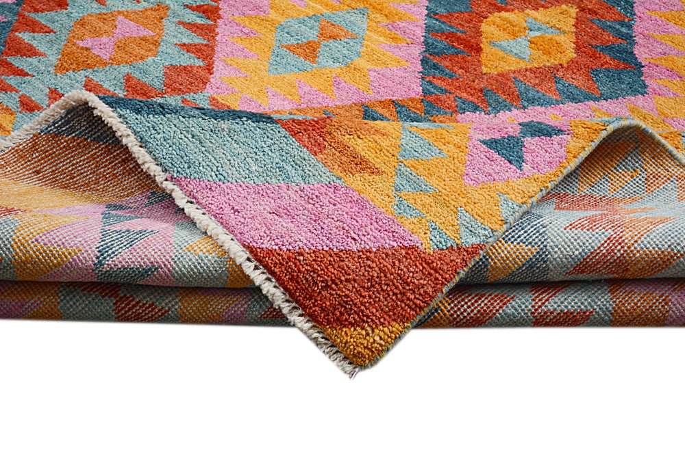 A handmade Afghan wool rug featuring a vibrant geometric pattern in pink, orange, and blue.