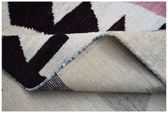 A corner of a handmade Afghan wool rug with a geometric pattern in dark brown and cream.