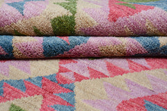 A handmade Afghan wool rug featuring a geometric pattern in shades of pink, blue, green, and cream.