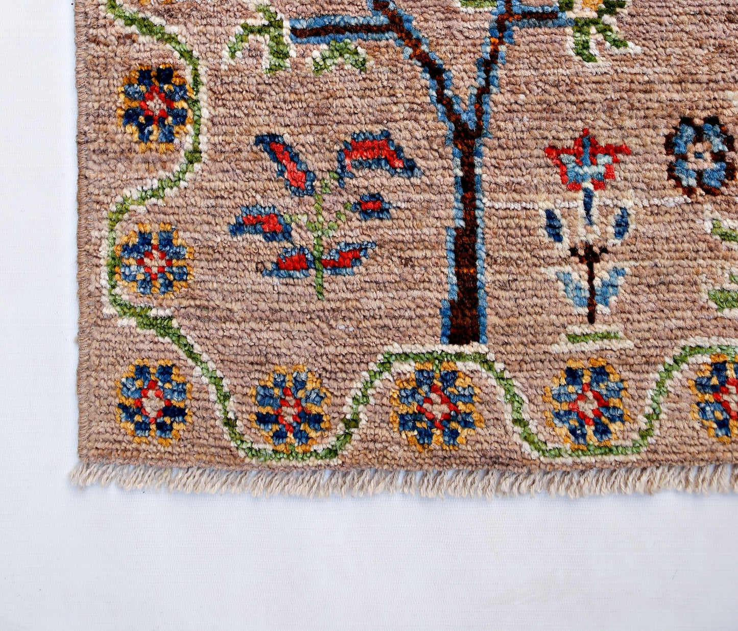 A handmade Afghan wool rug featuring a tan field with floral motifs and a decorative border.
