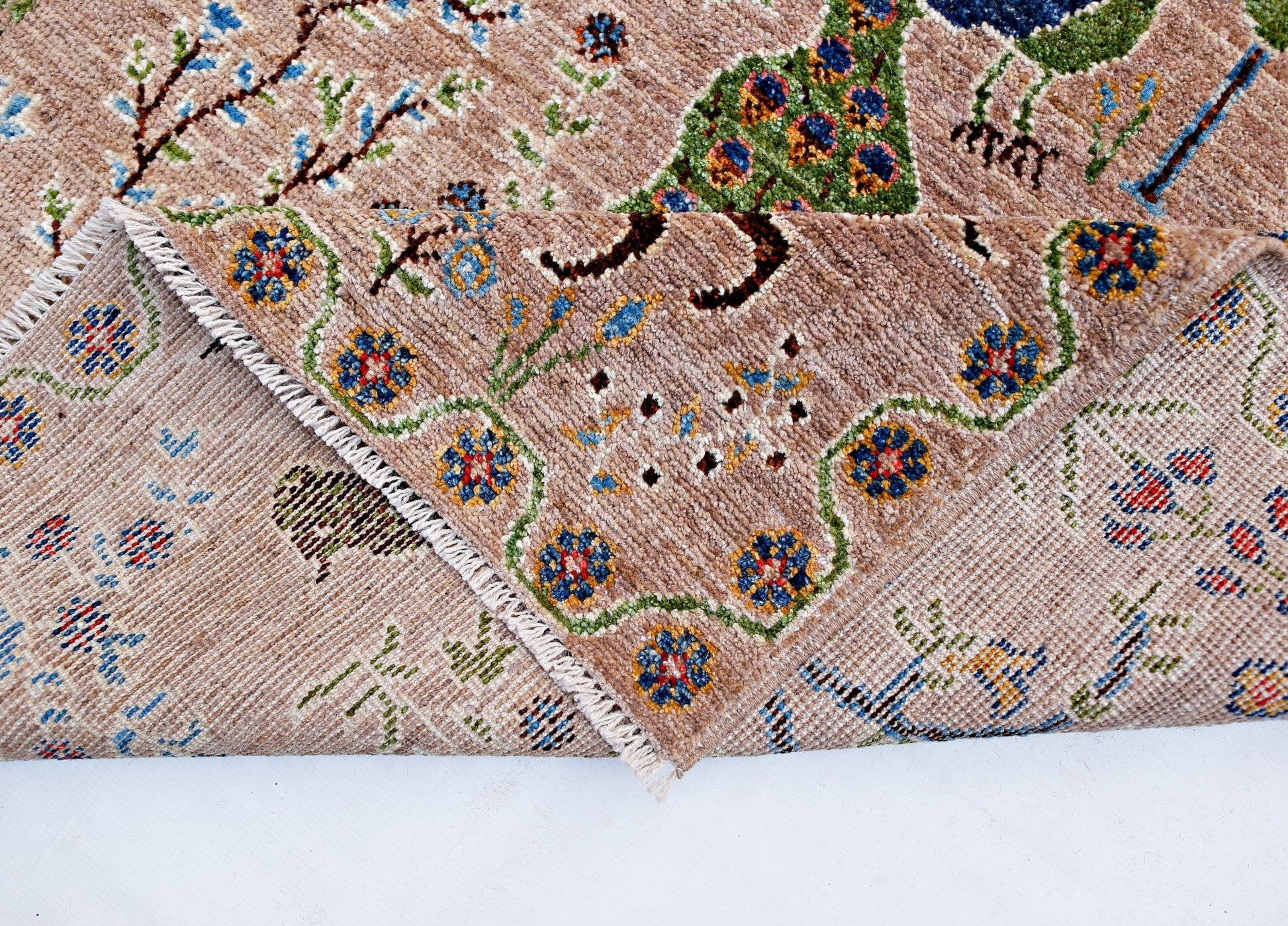 A handmade Afghan Pashm wool rug featuring a tan background with colorful floral and bird motifs.