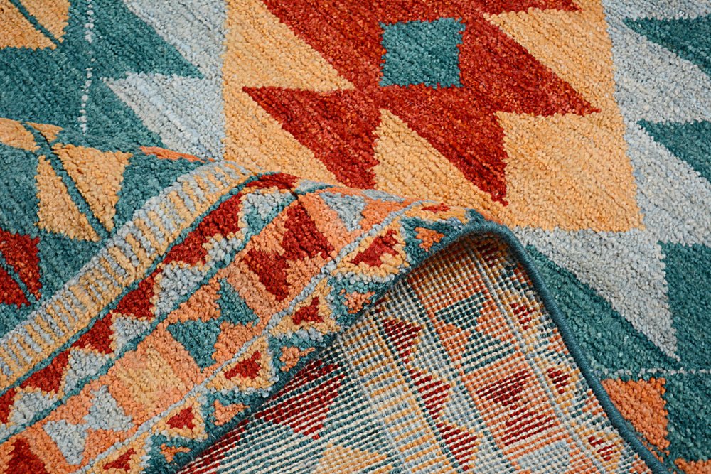 A handmade Afghan wool rug featuring a geometric pattern in teal, orange, and red.