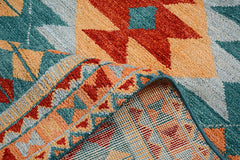A handmade Afghan wool rug featuring a geometric pattern in teal, orange, and red.