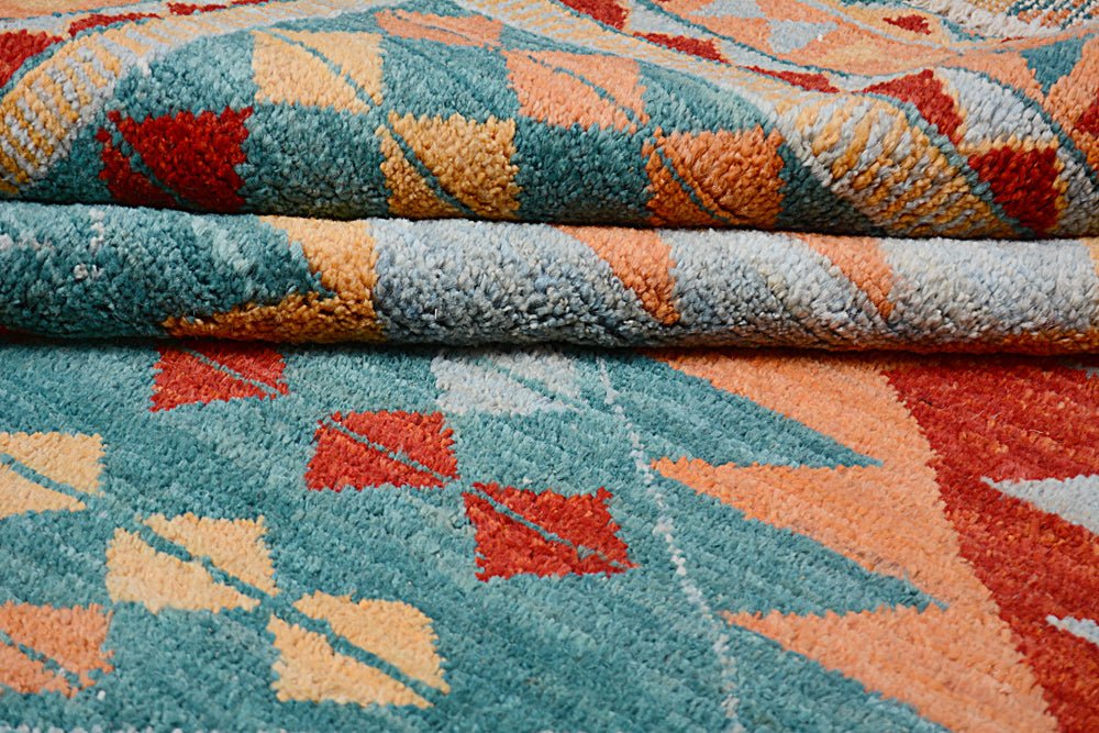 A handmade Afghan wool rug featuring a geometric pattern in teal, orange, and red.